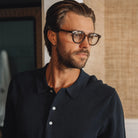 Man wearing glasses and a dark polo shirt indoors