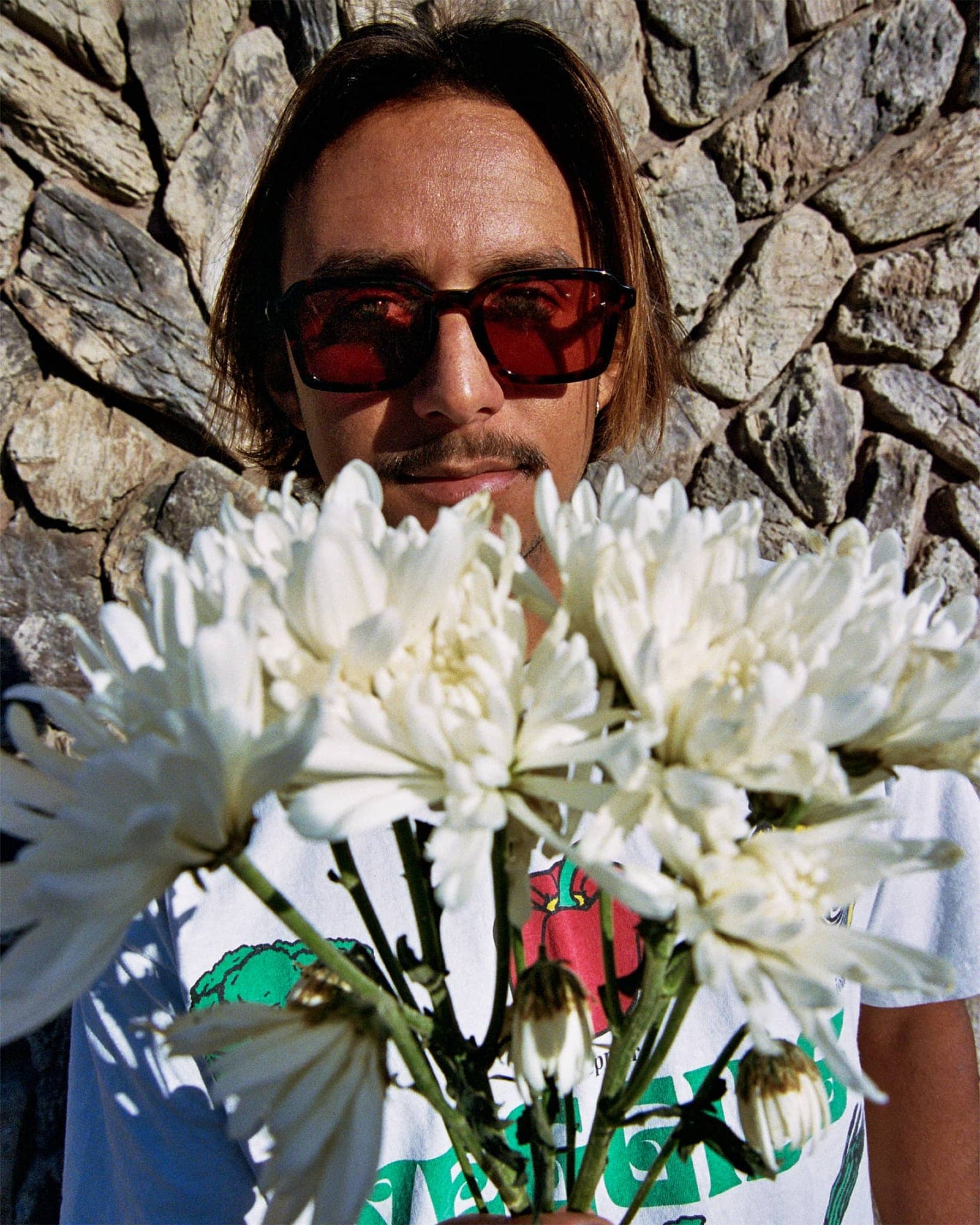 Person holding white flowers against a stone wall