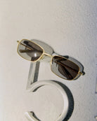 Gold-framed sunglasses with dark lenses on a textured white surface