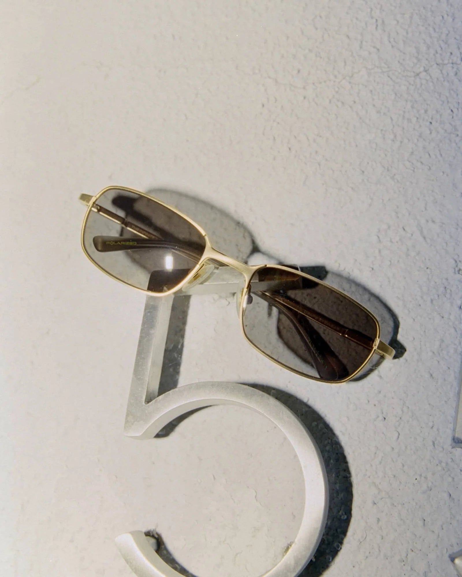 Gold-framed sunglasses with dark lenses on a textured white surface
