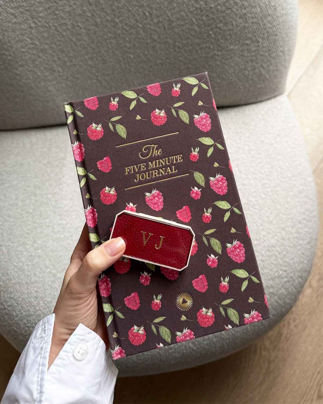 Five Minute Journal with dark brown cover featuring raspberry pattern and red leather VJ monogrammed clasp held by hand