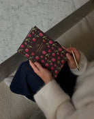 Person holding a burgundy floral patterned journal with gold pen, sitting on marble surface wearing cream sweater and navy pants