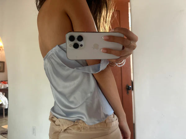 Person taking a mirror selfie with a phone, wearing a light blue top and beige shorts.