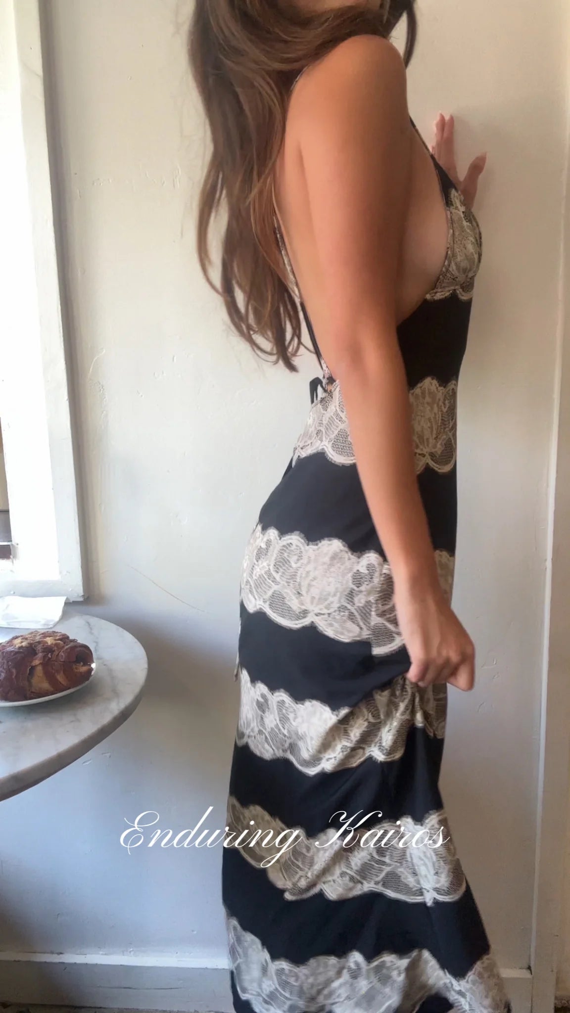 Woman wearing a black and white lace dress standing against a white wall.