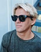 Man wearing sunglasses and a dark shirt against a light blue background