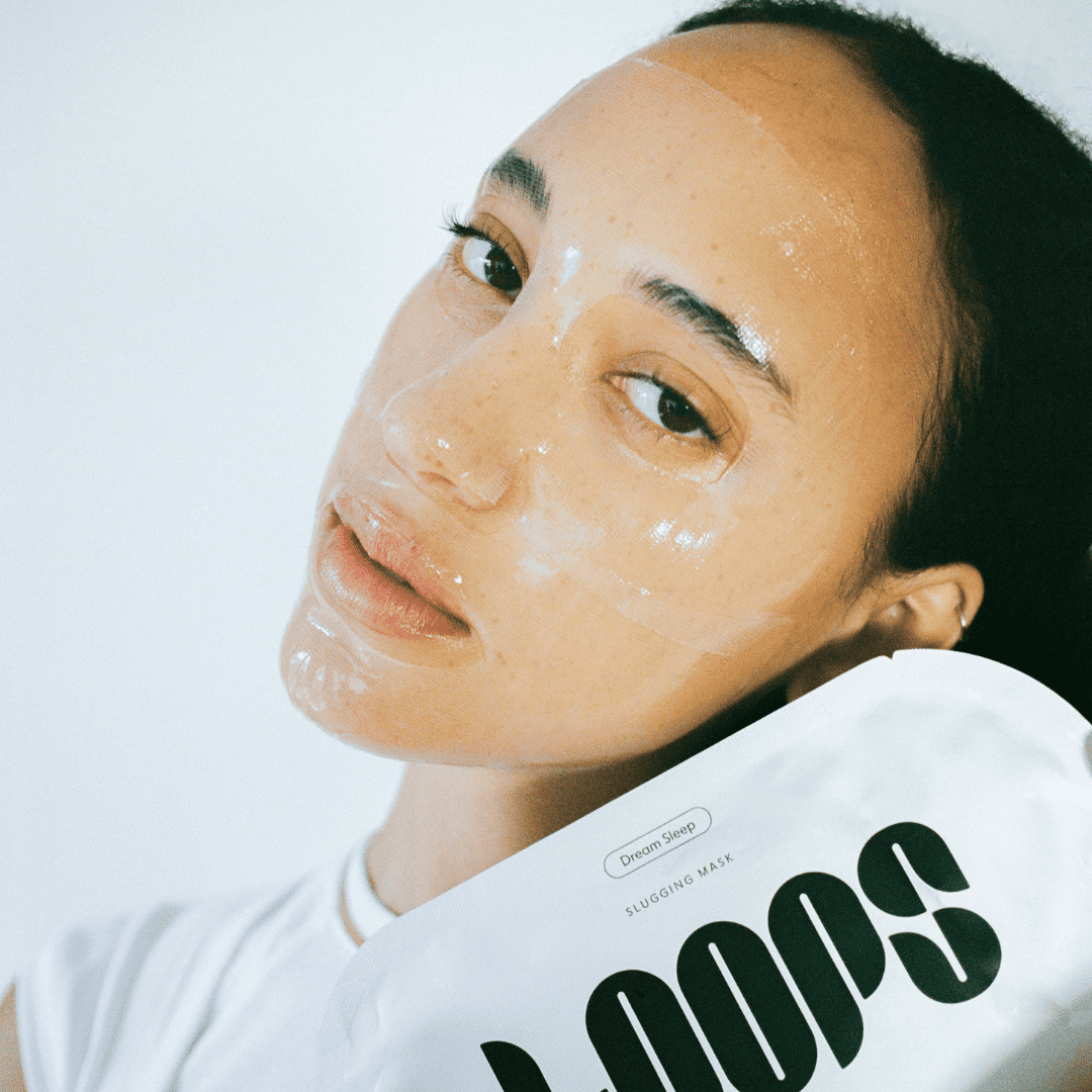 Woman with glowing skin holding white Olbia Dream Sleep slugging mask package with dark green logo