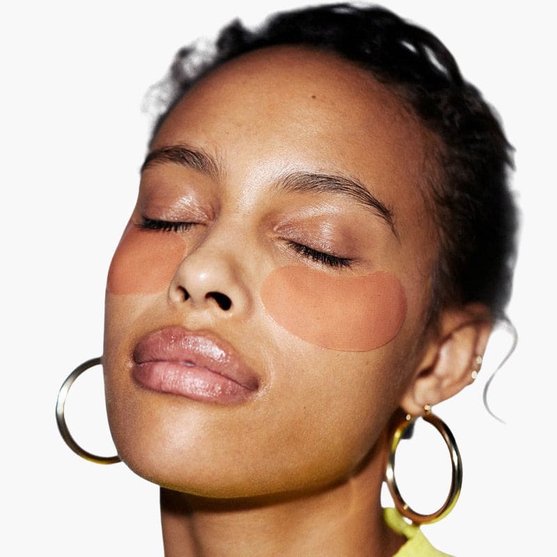 Gold hoop earrings worn by model with glowing skin and eyes closed against white background