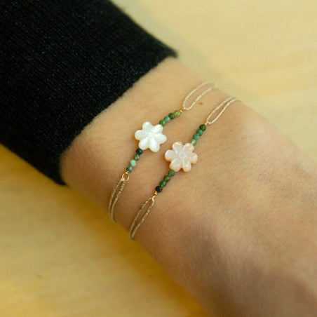 Delicate gold chain bracelet with white flower charm and green beads on wrist against yellow background
