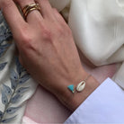 Delicate gold chain bracelet with turquoise tassel charm and cowrie shell on wrist, shown with matching stacked rings