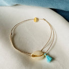 Gold chain anklet with cowrie shell and turquoise tassel charm on beige fabric display