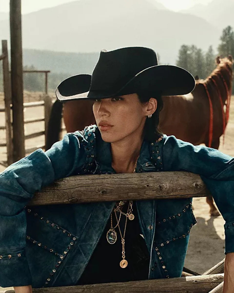 Black wide-brim cowboy hat worn by model in western ranch setting with teal studded jacket