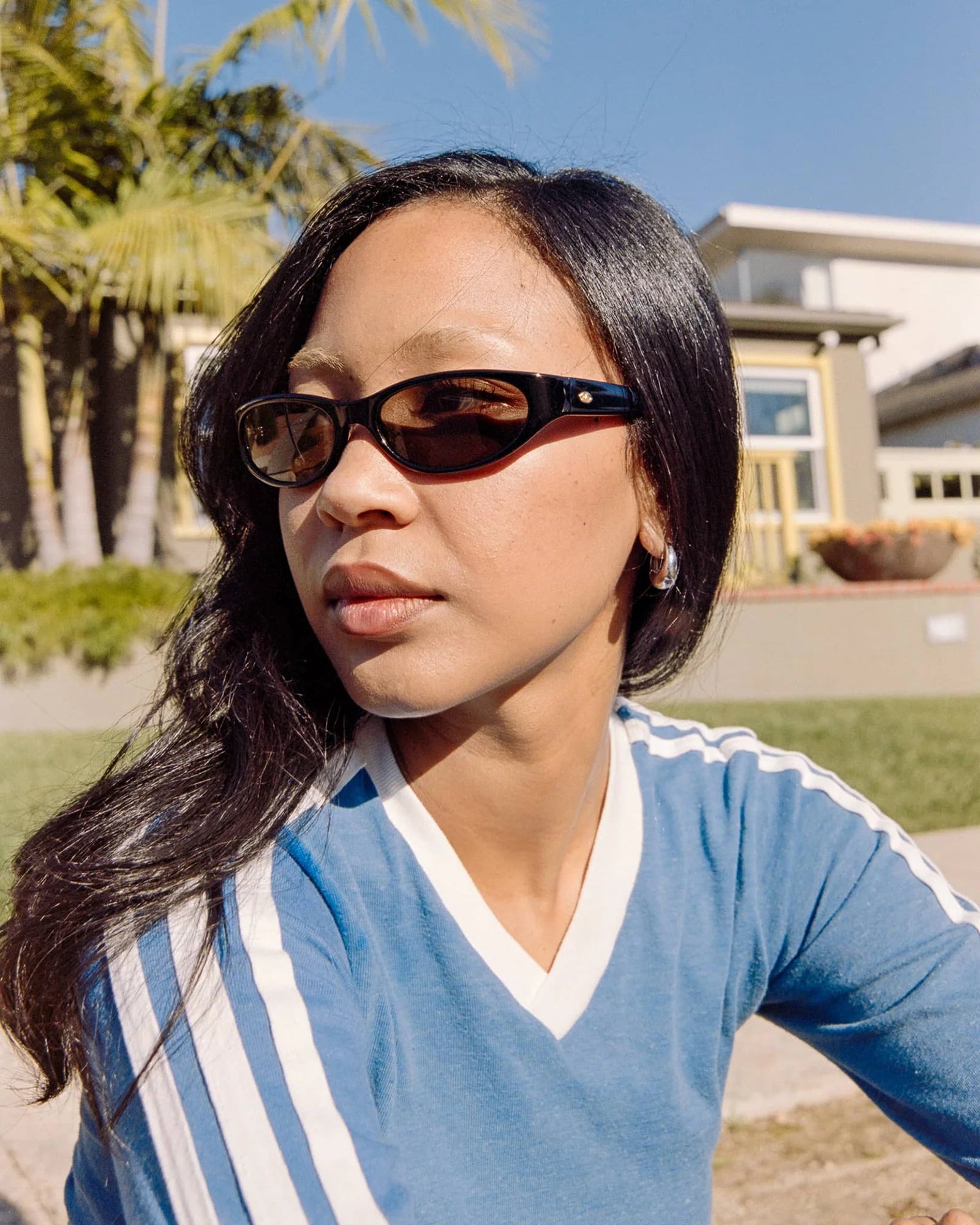 Woman wearing sunglasses and a blue shirt with white stripes outdoors