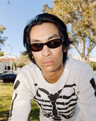 Person wearing sunglasses and a white sweater with black designs outdoors