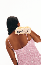 Yellow beaded handbag with embroidered 'merci' text and smile detail on beige canvas base, worn on shoulder with pink sequin dress