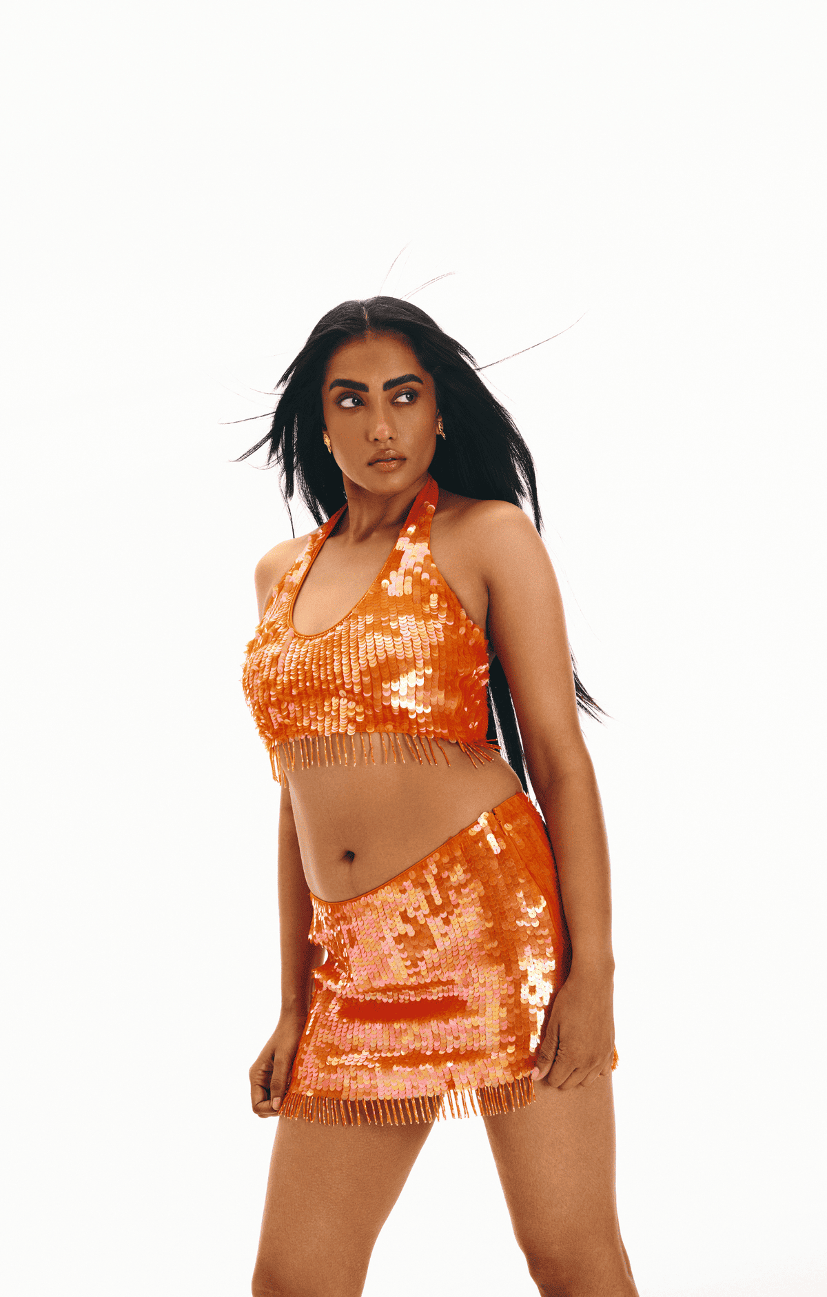 Orange sequin two-piece set with halter crop top and mini skirt featuring fringe trim details