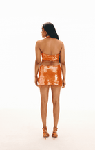 Orange sequined two-piece set with halter crop top and mini skirt featuring beaded fringe trim