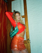 Woman in orange sequin crop top and skirt set with teal sequin sleeves posing in doorway
