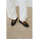 Black mesh Mary Jane flats with ankle strap worn with white wide-leg pants on beige carpet