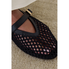 Black mesh Mary Jane flat with ankle strap and brown leather lining on beige carpet