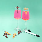 Two champagne flutes with pink liquid and small figures on a teal background