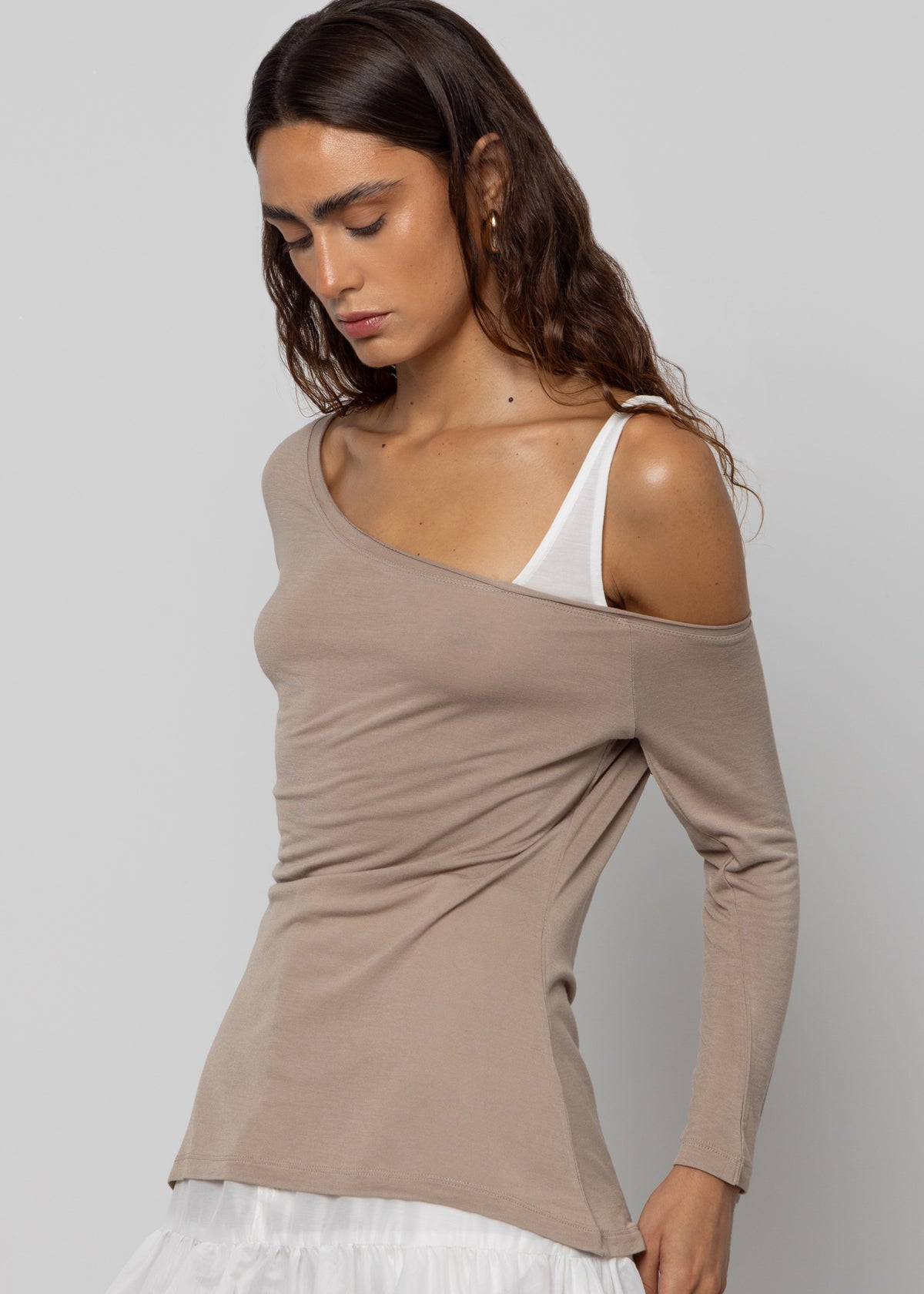 Taupe asymmetric cold-shoulder long sleeve top with one-shoulder cutout, layered over white tank and skirt.