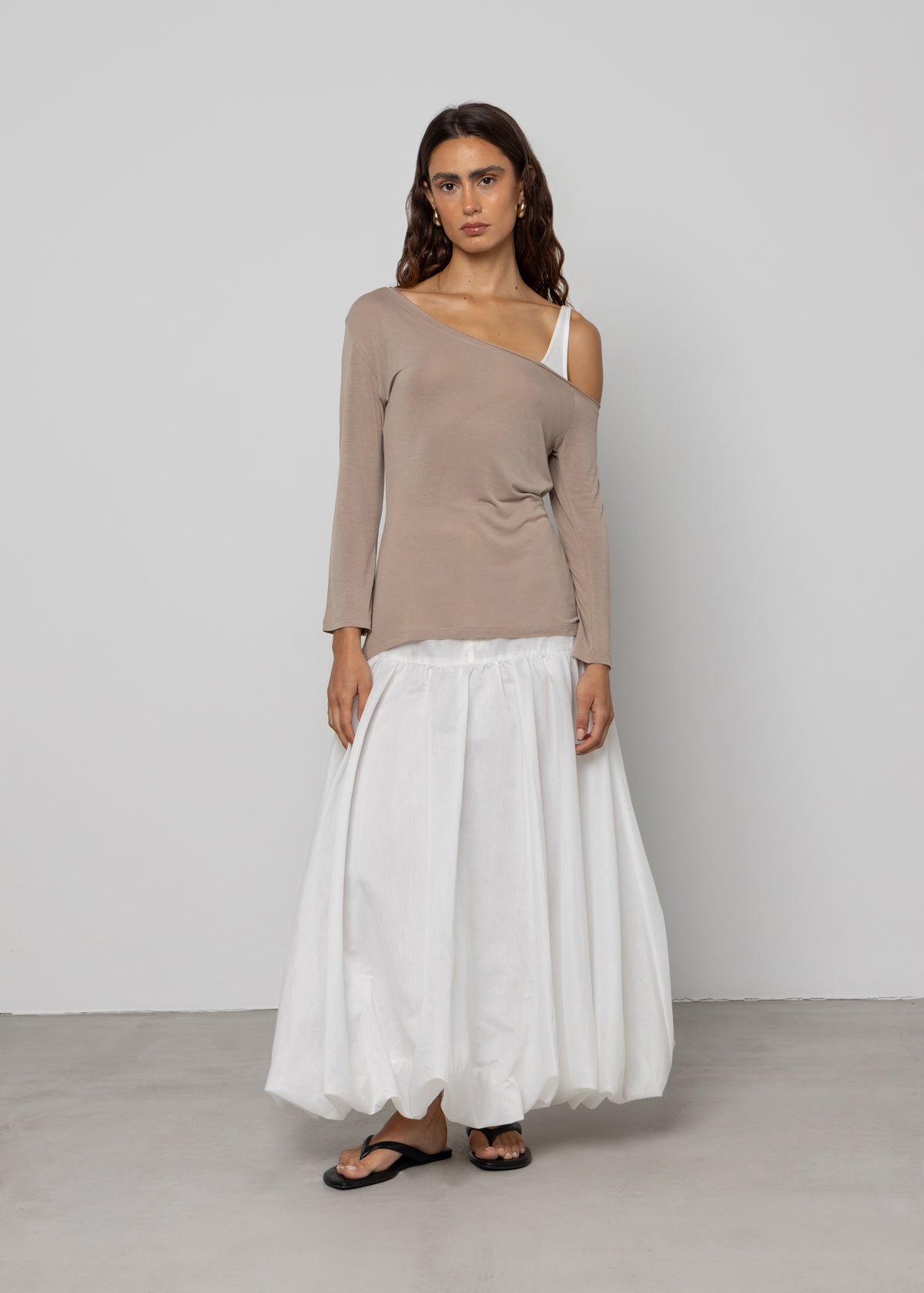 Asymmetric off-shoulder taupe long-sleeve top with white bra strap detail, paired with white bubble maxi skirt.