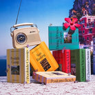 Vintage cream-colored portable radio with books about Italian coastal destinations arranged on sandy beach with blue sky