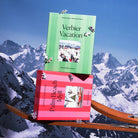 Two puzzle boxes - green "Verbier Vacation" and pink "Palm Beach Idyll" - displayed against snowy mountain backdrop with ski tips.
