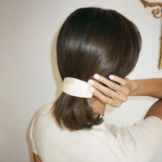 Ivory satin hair barrette held against dark brown hair, showing smooth rectangular shape and lustrous finish
