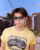 Person wearing sunglasses and a yellow t-shirt with text in an outdoor setting