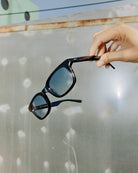 Person holding a pair of sunglasses against a reflective surface