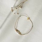 Delicate gold chain bracelet with three white pearls and small gold charm on white fabric background