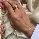 Gold twisted band ring and delicate pearl bracelet on hand against ivory silk fabric with pink flowers