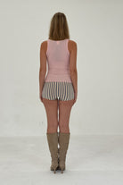 Woman wearing pink ribbed knit tank top and striped shorts with tan suede knee-high boots, rear view