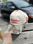 Beige baseball cap with camouflage brim featuring red embroidered text "Thriffland 76 Main St Sag Harbor, NY"