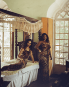 Two women in leopard print maxi dresses in vintage bedroom with ornate four-poster bed and arched windows