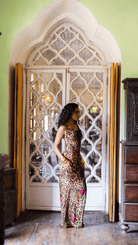 Woman in leopard print maxi dress with floral embellishments standing in ornate doorway with carved lattice details
