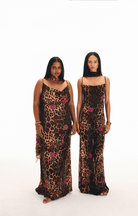 Two models wearing leopard print velvet maxi dresses with pink floral embroidery and spaghetti straps on white background