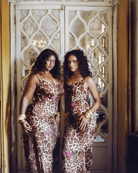Two women in leopard print slip dresses with floral embroidery and gold cuff bracelets standing by ornate mirrored doors