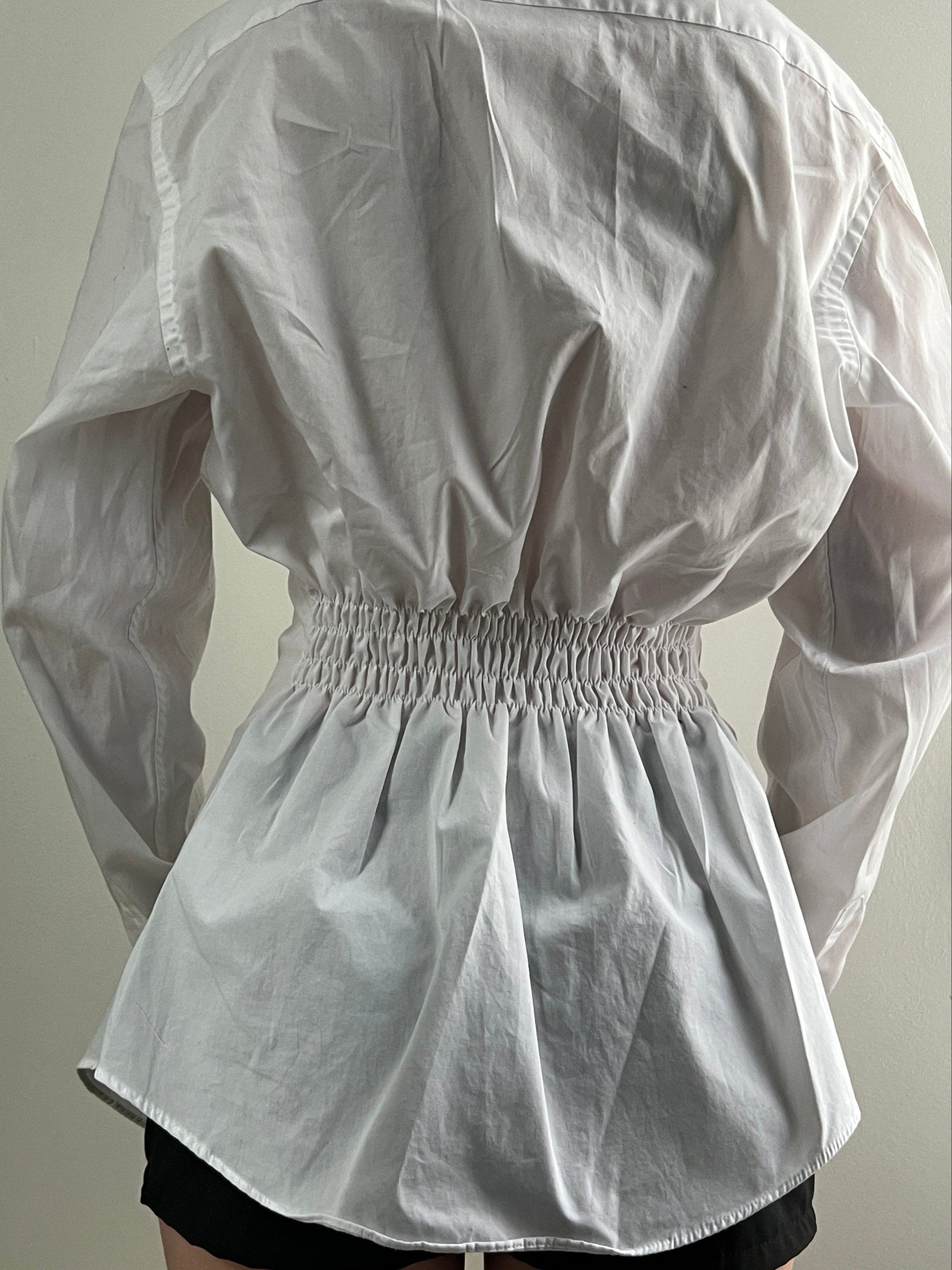 White long-sleeve shirt with elastic smocked waist creating gathered peplum silhouette, shown from back view