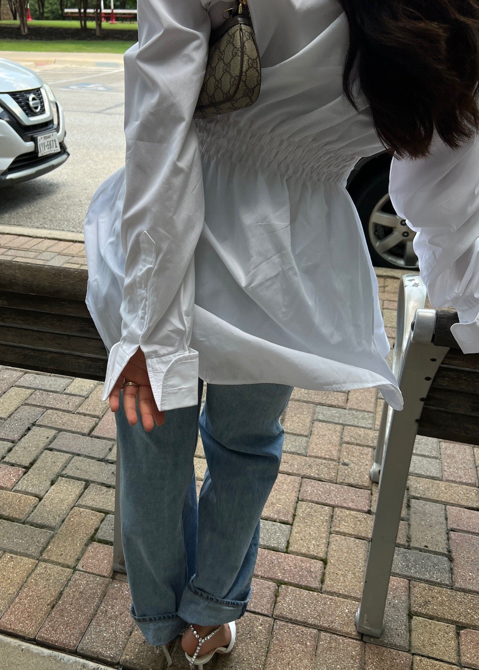 Person wearing oversized white button-up shirt with gathered waist detail, light blue jeans, and designer monogram shoulder bag