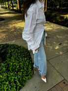 Woman wearing oversized white button-down shirt with light wash denim jeans and white pointed-toe heels in outdoor setting