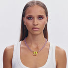 Purple beaded necklace with yellow butterfly pendant on model wearing white ribbed tank top
