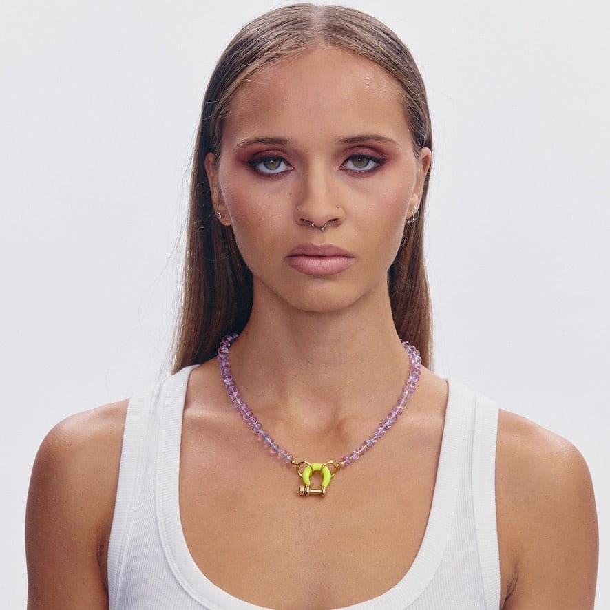 Purple beaded necklace with yellow butterfly pendant on model wearing white ribbed tank top