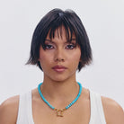 Turquoise beaded necklace with gold shackle clasp pendant on white tank top
