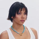 Turquoise beaded necklace with gold shackle clasp pendant on white tank top
