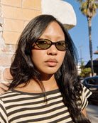Woman wearing tortoiseshell brown oval sunglasses with tinted lenses in black and white striped shirt outdoors