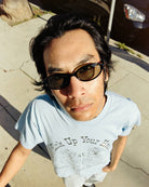 Person wearing light blue t-shirt with sunglasses taking selfie outdoors on sunny day