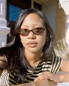 Woman wearing brown oval-frame sunglasses with dark tinted lenses in natural sunlight, black and white striped shirt