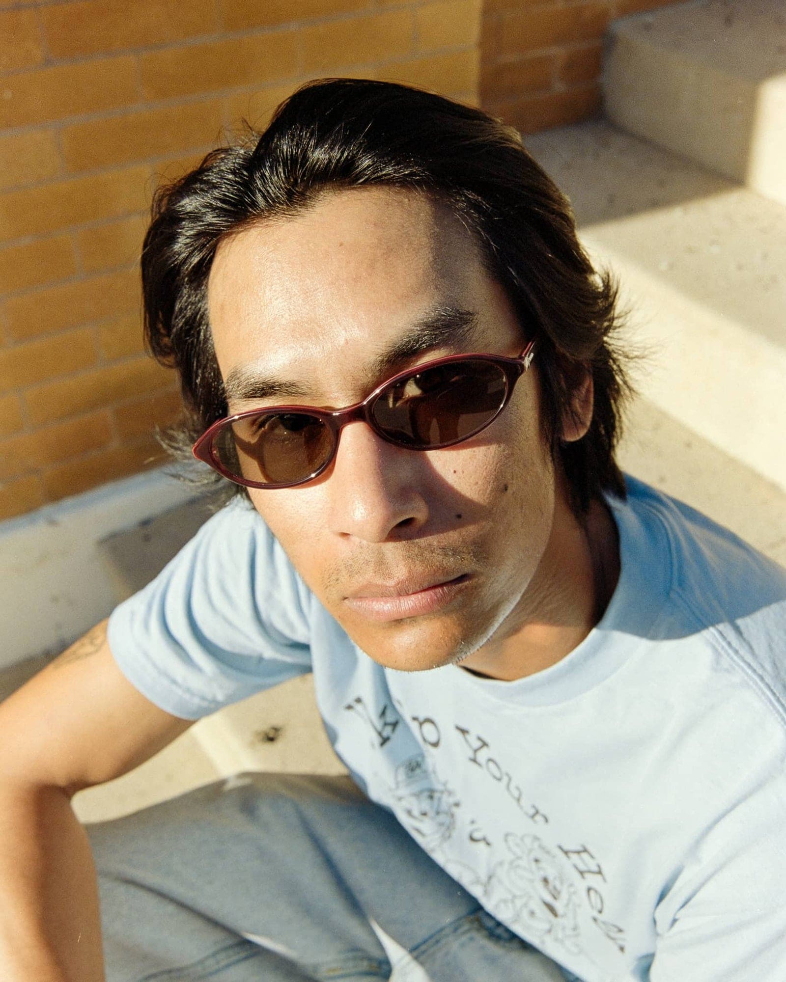 Person wearing red oval sunglasses and light blue t-shirt, shot from above in natural sunlight